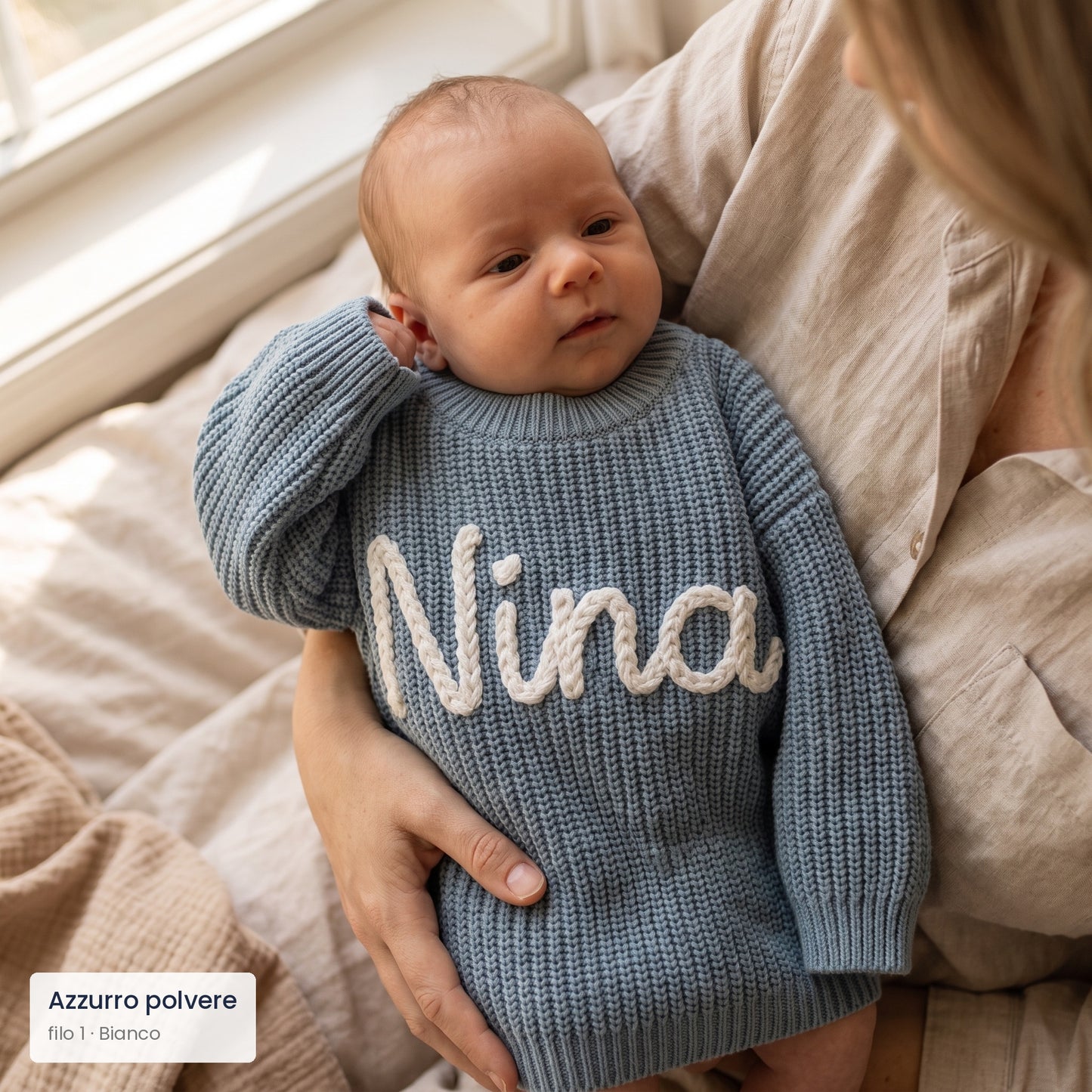 Neonata in braccio alla mamma con maglioncino azzurro polvere e nome Nina